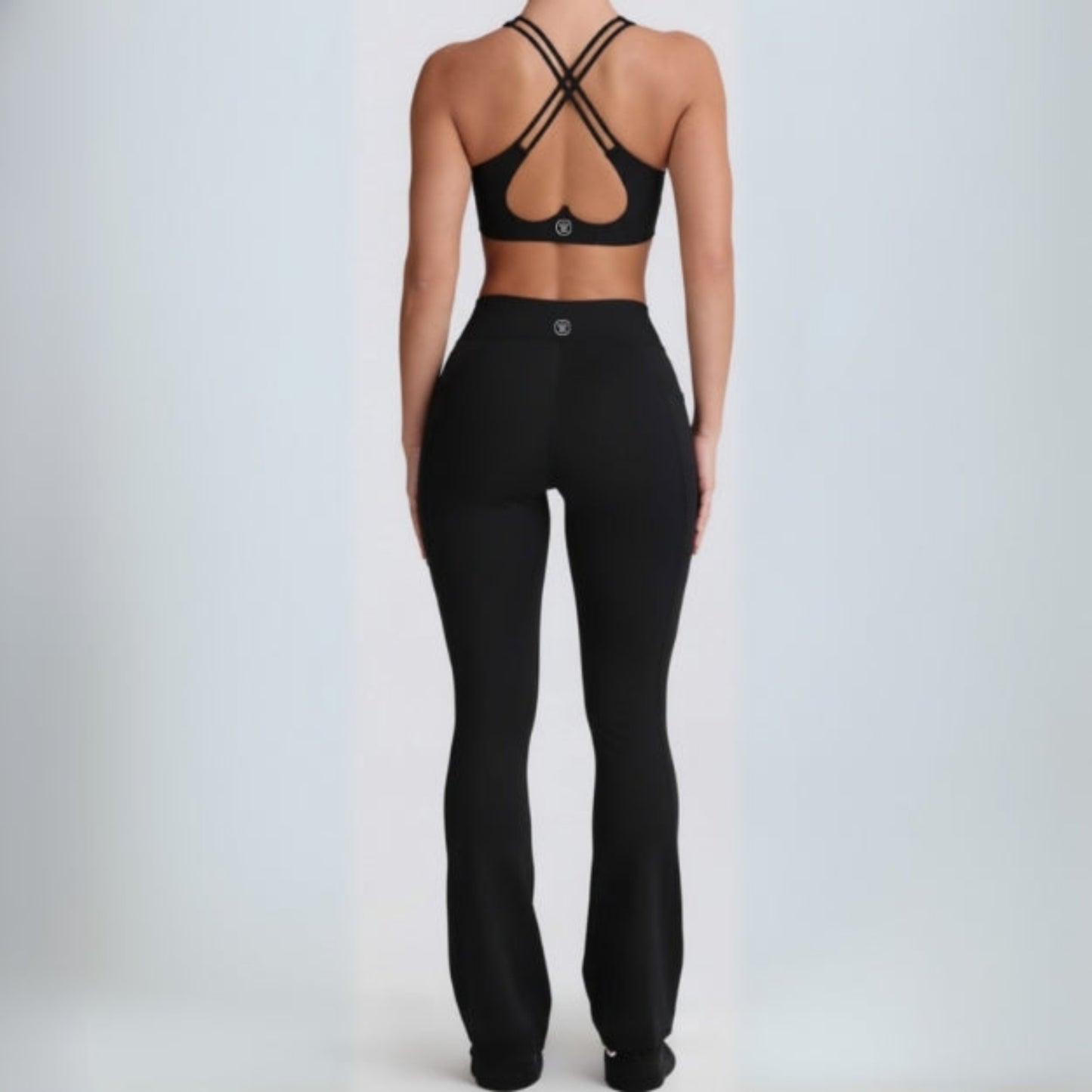 Person wearing a black  black dew flow fit flares sports bra and leggings on a light gray background