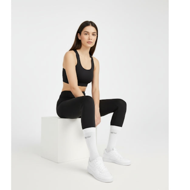 Woman sitting, wearing black seamless sports bra, black seamless leggings, white DEW crew socks, and sneakers. Athleisure style look.