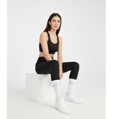 Woman sitting, wearing black seamless sports bra, black seamless leggings, white DEW crew socks, and sneakers. Athleisure style look.