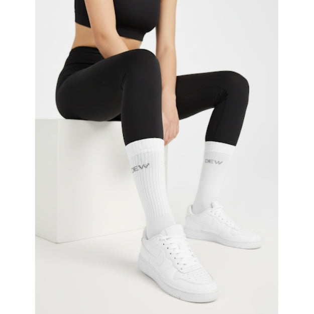 Close-up of white crew socks with DEW logo, black seamless leggings, and white sneakers. Activewear styling detail.