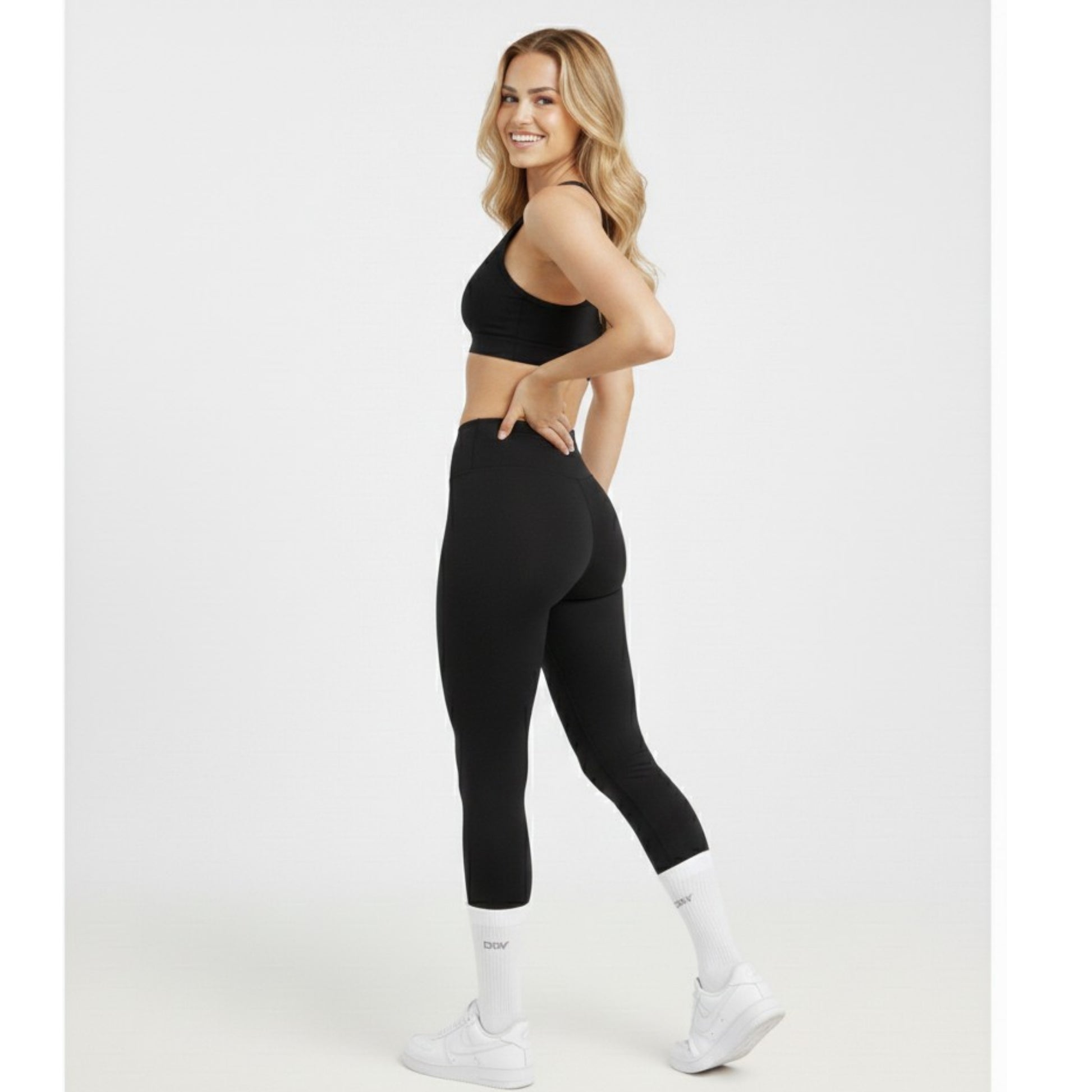 Woman wearing a black athletic outfit with white socks on a white background 