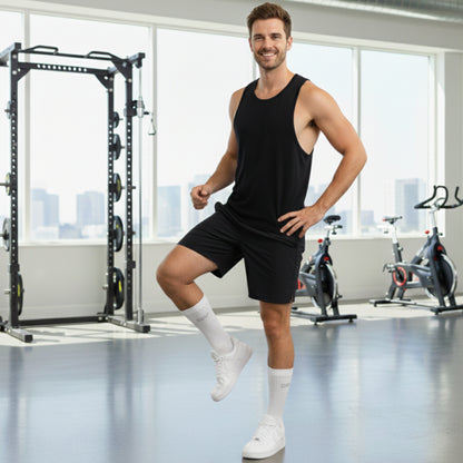 Man wearing Dew white socks and in black tank top and shorts posing in a gym with exercise equipment in the background
