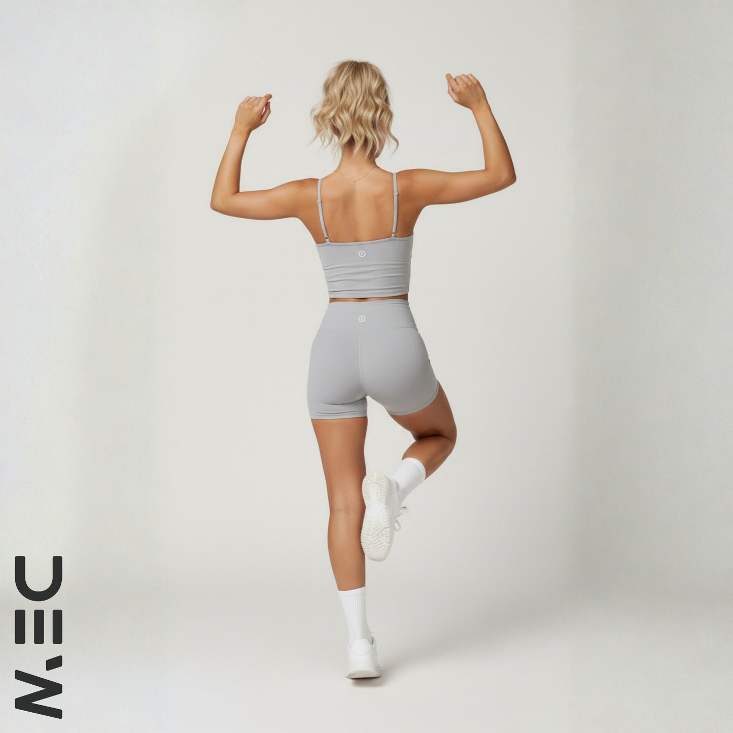 Woman in gray dew luxe cami and shorts flexing muscles on a white background with 'NIN' logo.