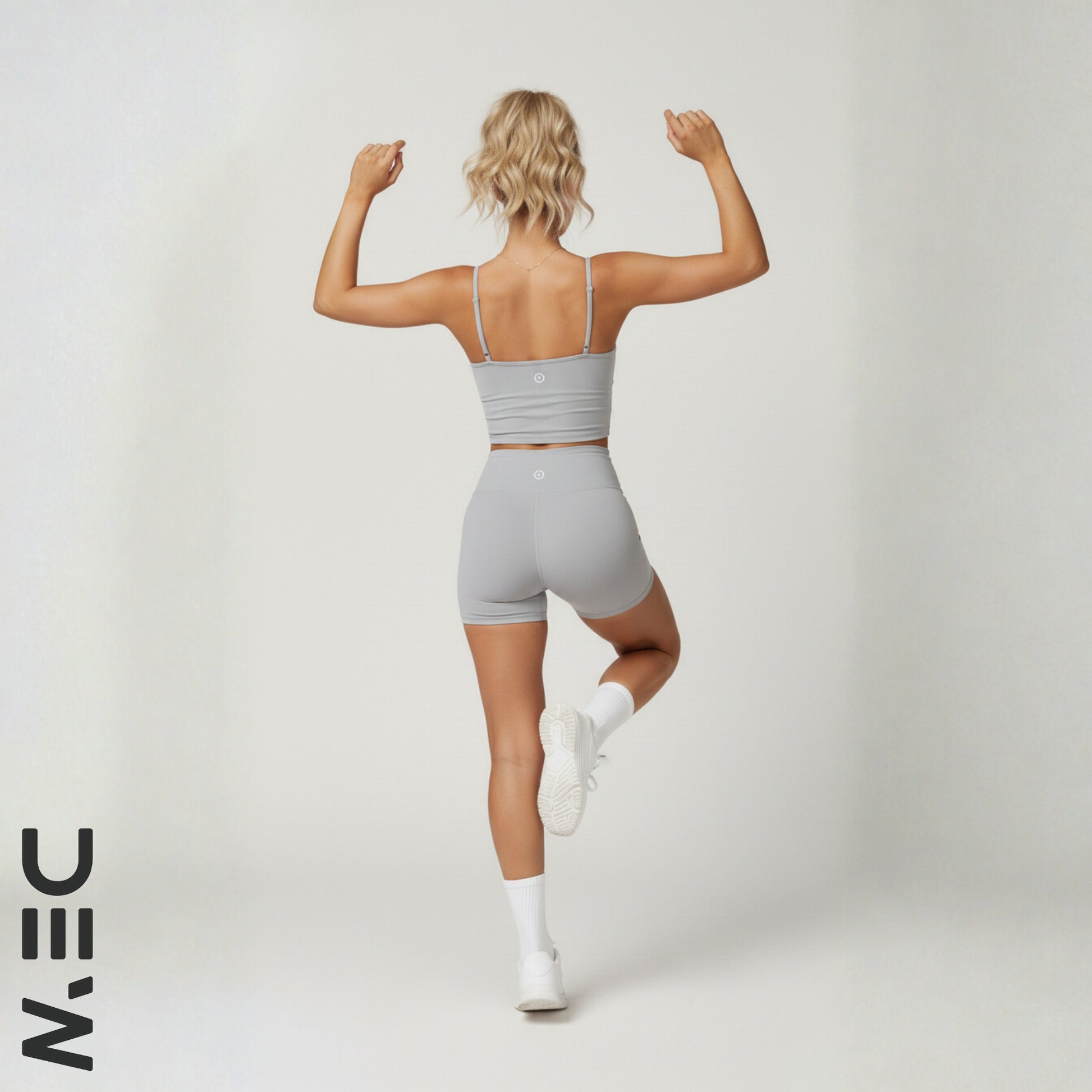Woman in gray dew luxe cami and shorts flexing muscles on a white background with 'NIN' logo.