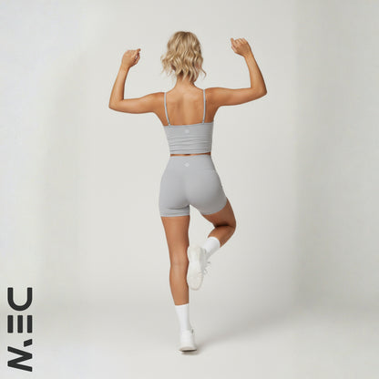 Woman in gray dew luxe cami and shorts flexing muscles on a white background with 'NIN' logo.