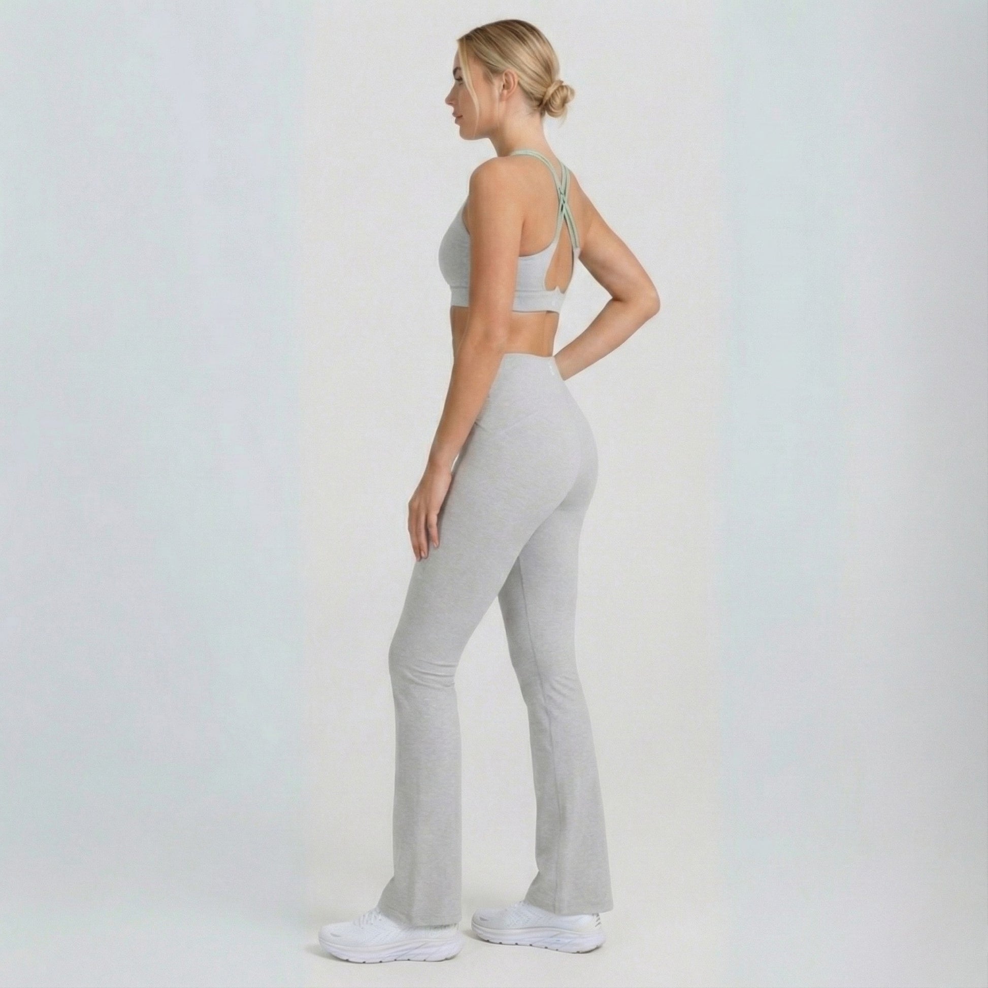 Woman wearing a gray sports bra and Dew Flow fit flares leggings on a white background
