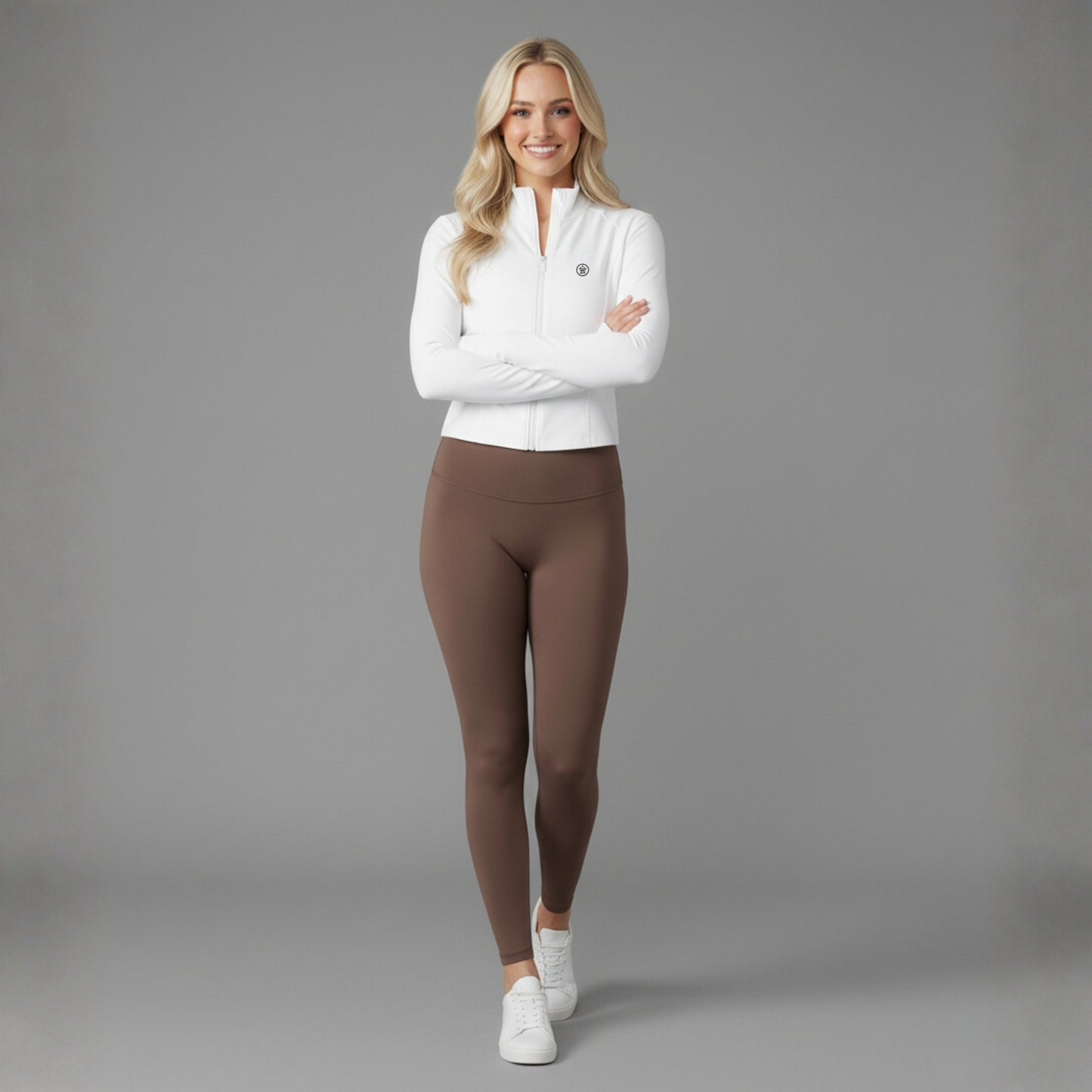 Woman wearing a white Dew Flex UPF50+ Performance jacket and brown leggings on a gray background