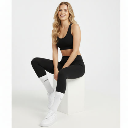 Woman wearing white dew 100% bamboo socks, black sports bra and leggings with white sneakers on a white background